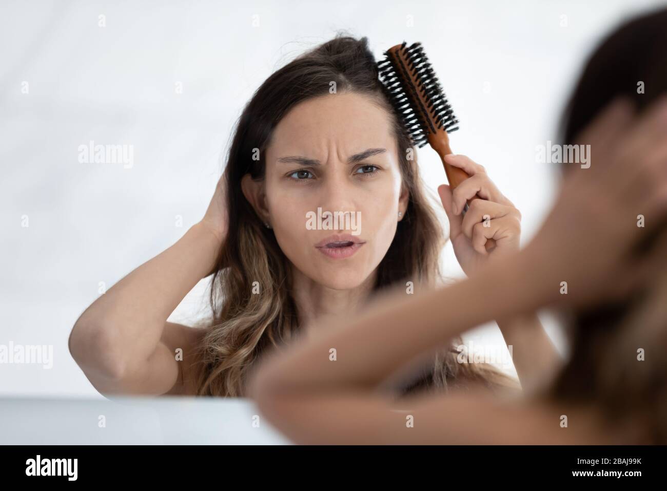 Woman looks in mirror combing hair feels dissatisfied hair condition Stock Photo