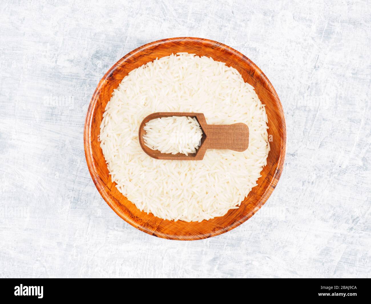 Indian long grain Basmati rice in brown wooden bowl and in scoop on white concrete background Stock Photo
