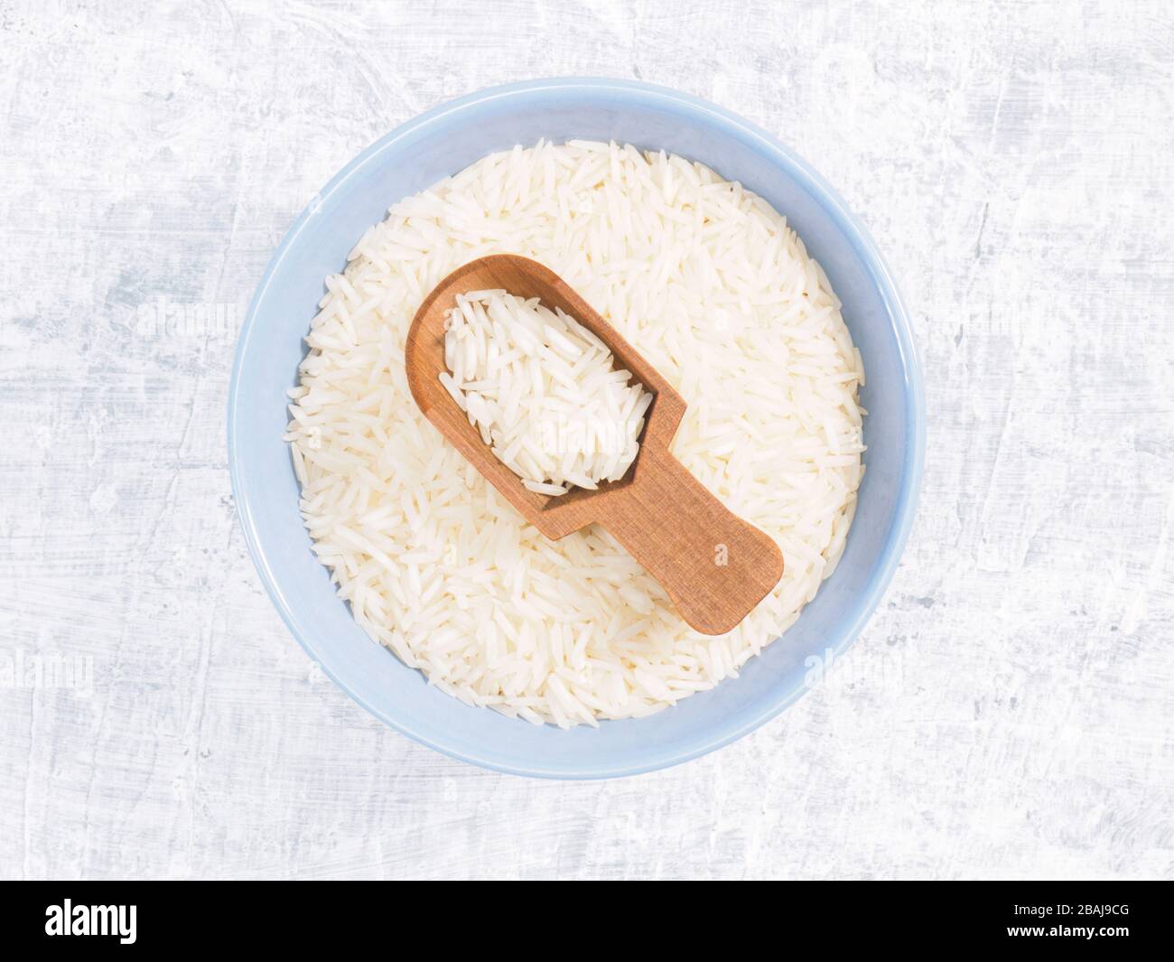 Indian long grain Basmati rice in blue ceramic bowl and wooden scoop on white concrete background Stock Photo