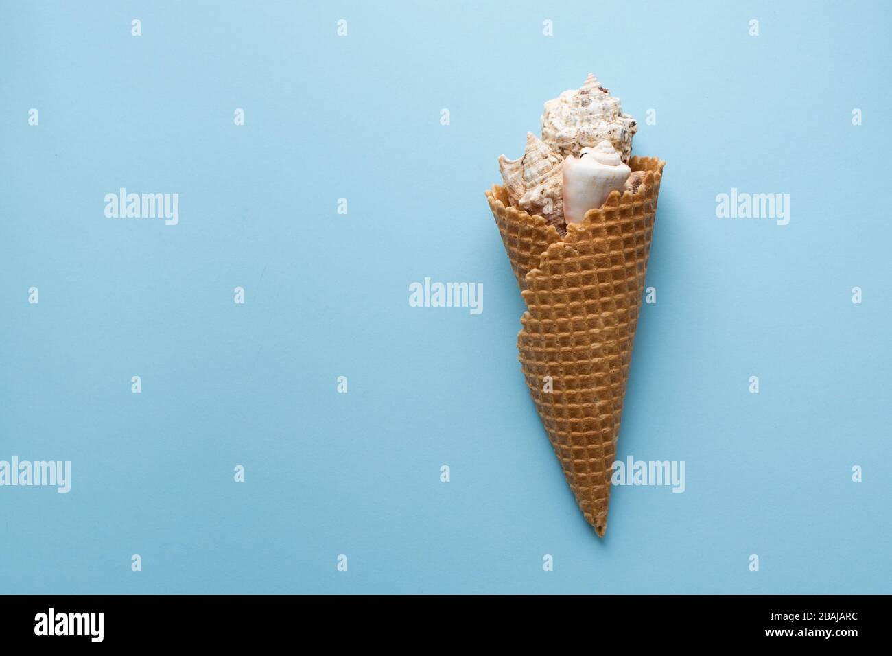 Creative composition with seashell and ice cream cone on pastel blue