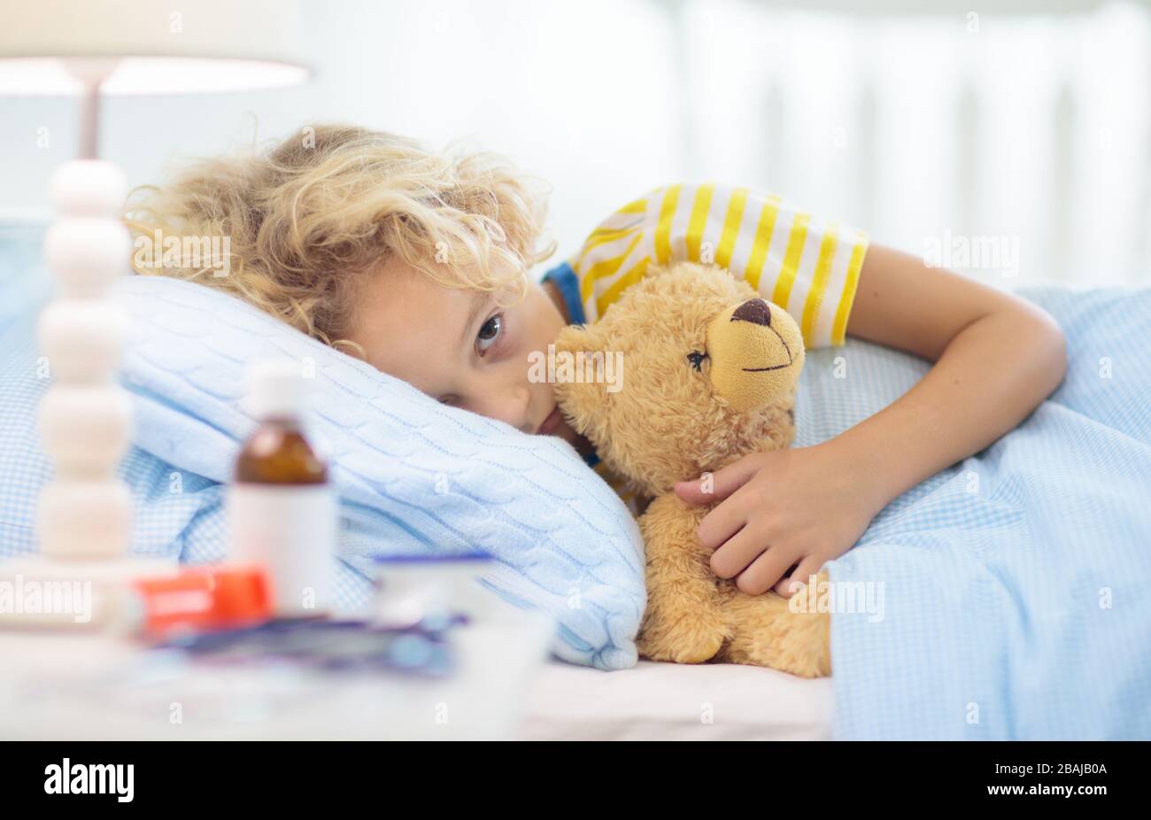 Sick little boy with asthma medicine. Ill child lying in bed. Unwell kid with chamber inhaler for cough treatment. Flu season. Bedroom or hospital roo Stock Photo