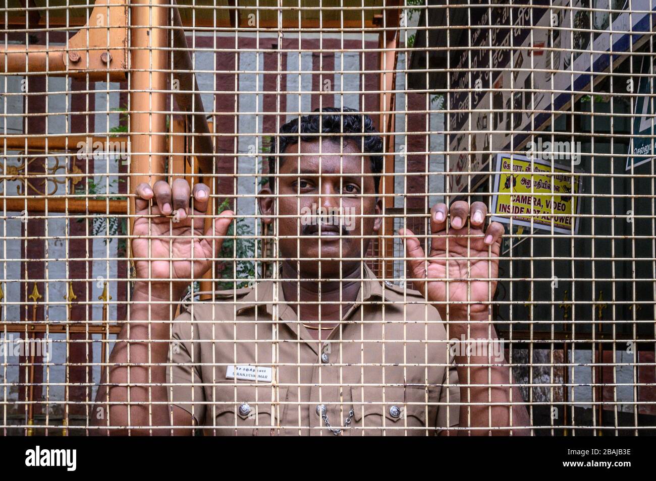Portrait of a security man behind wire mesh at Arulmigu Koodal Azhagar Temple, Madurai, India Stock Photo