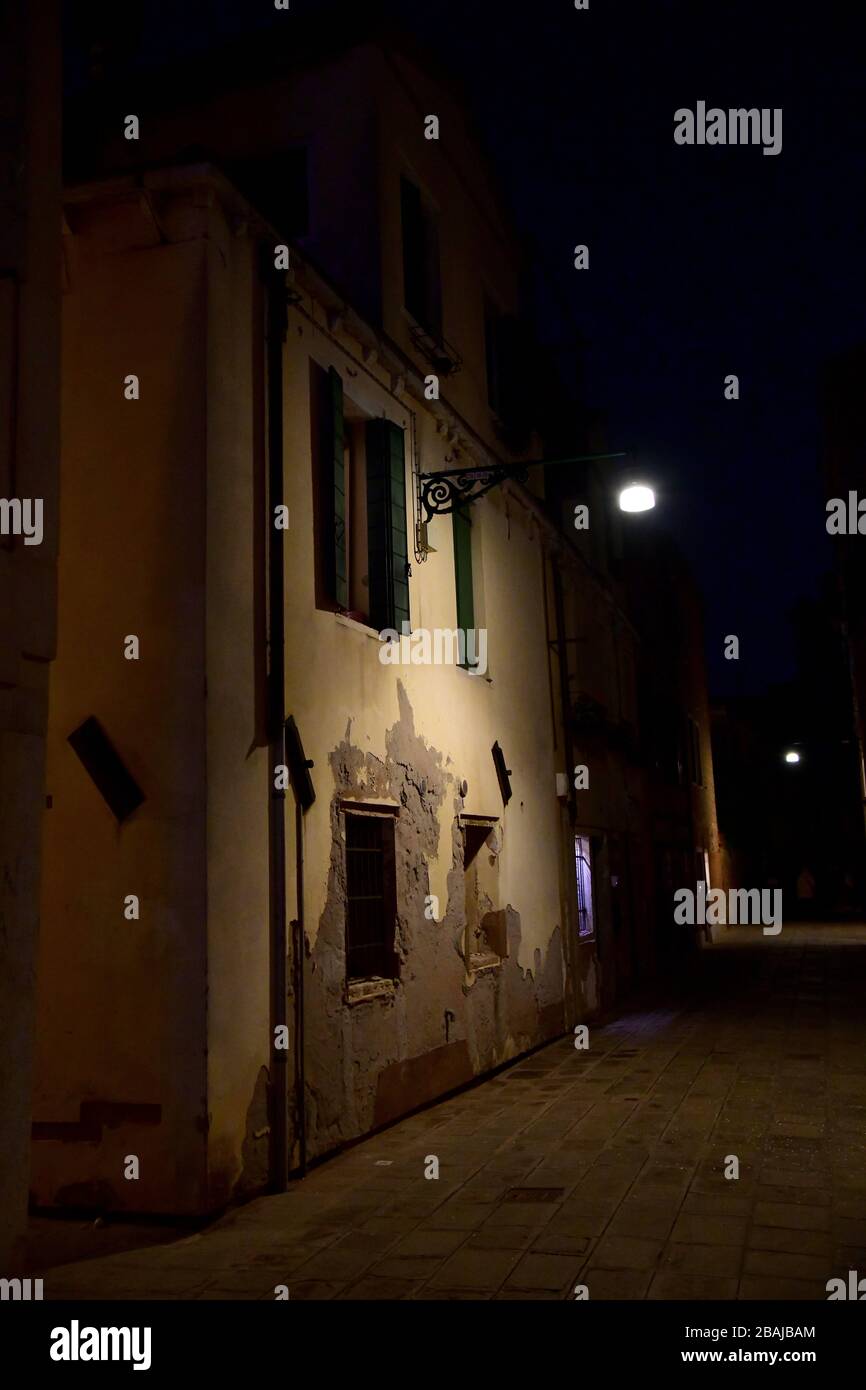 Retro lamp on Venetian home giving ample light in dark alley against the backdrop of a traditional house basically covered in the dark with only light Stock Photo