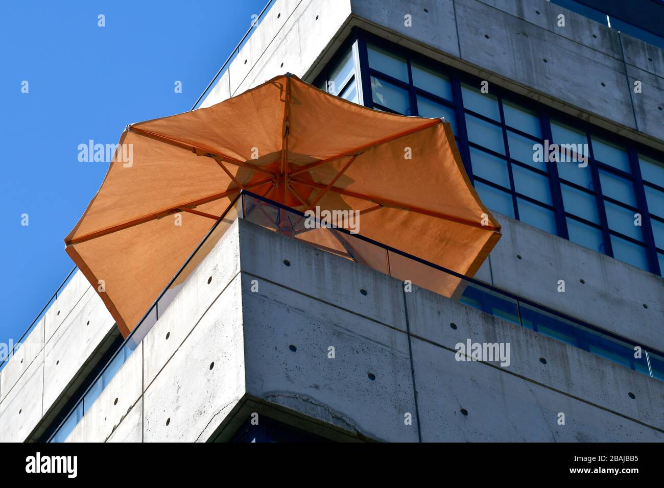 Low angle view of a corner section of a minimalistic grey concrete building with a bright orange sun umbrella stick Stock Photo