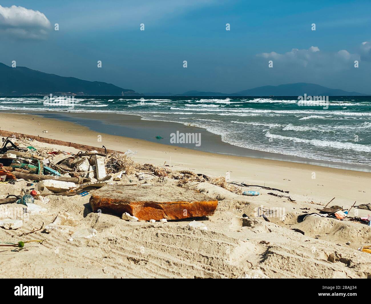 Discarded garbage on the shore of a beautiful sandy beach, sea waves. Plastic, bottles, environmental pollution bags. Ecological problem. Sea shore wi Stock Photo