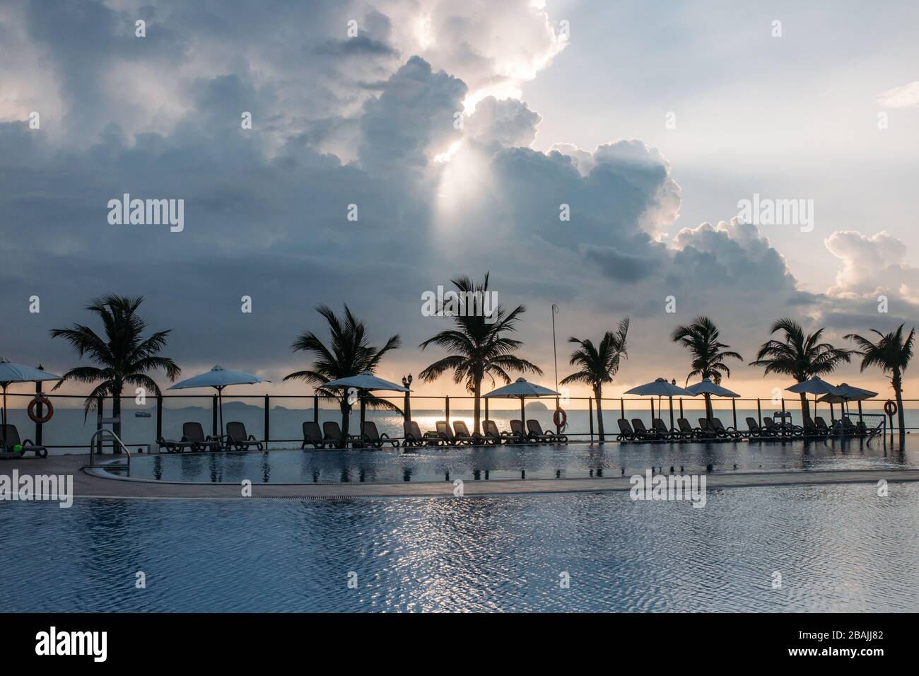 Swimming pool, palm trees around, reflection of palm trees in the pool, dawn with a beautiful cloudy sky. An empty area with many sunbeds, the sun pas Stock Photo
