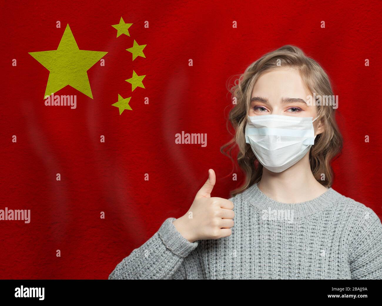 Happy woman in face mask holding thumb up on national flag China. Flu epidemic and virus protection concept Stock Photo