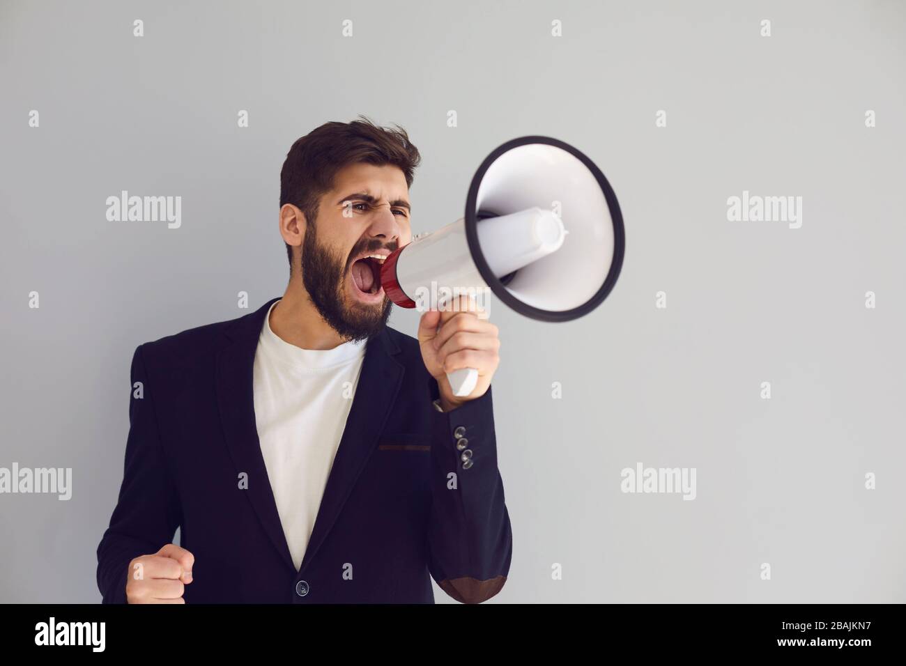 Man with a loudspeaker shouts announces news protest on a gray background. Stock Photo