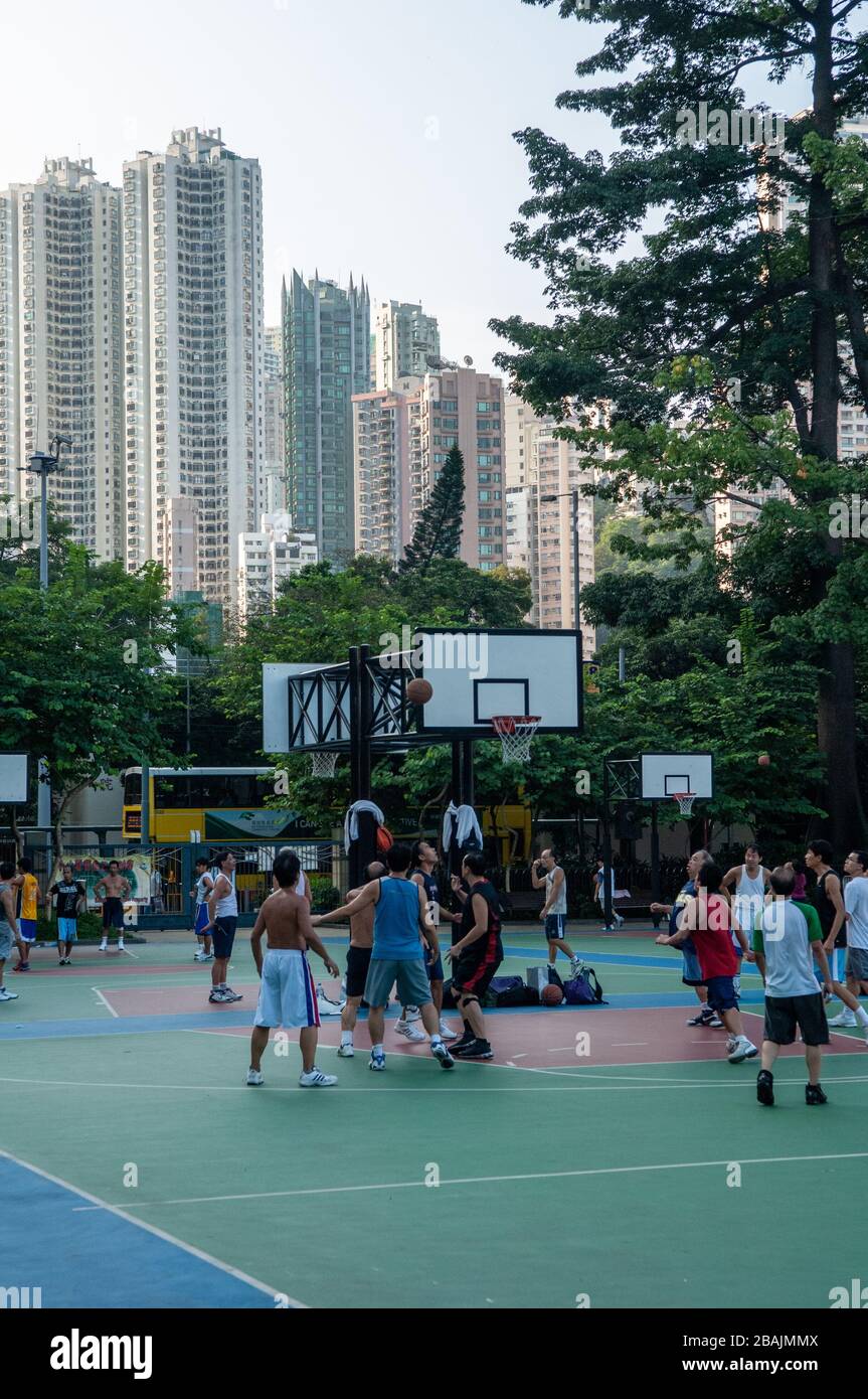 Young men exercising in Victoria Park, Hong Kong, on an all weather surface, playing basketball. With tall buildings forming the backdrop. Stock Photo