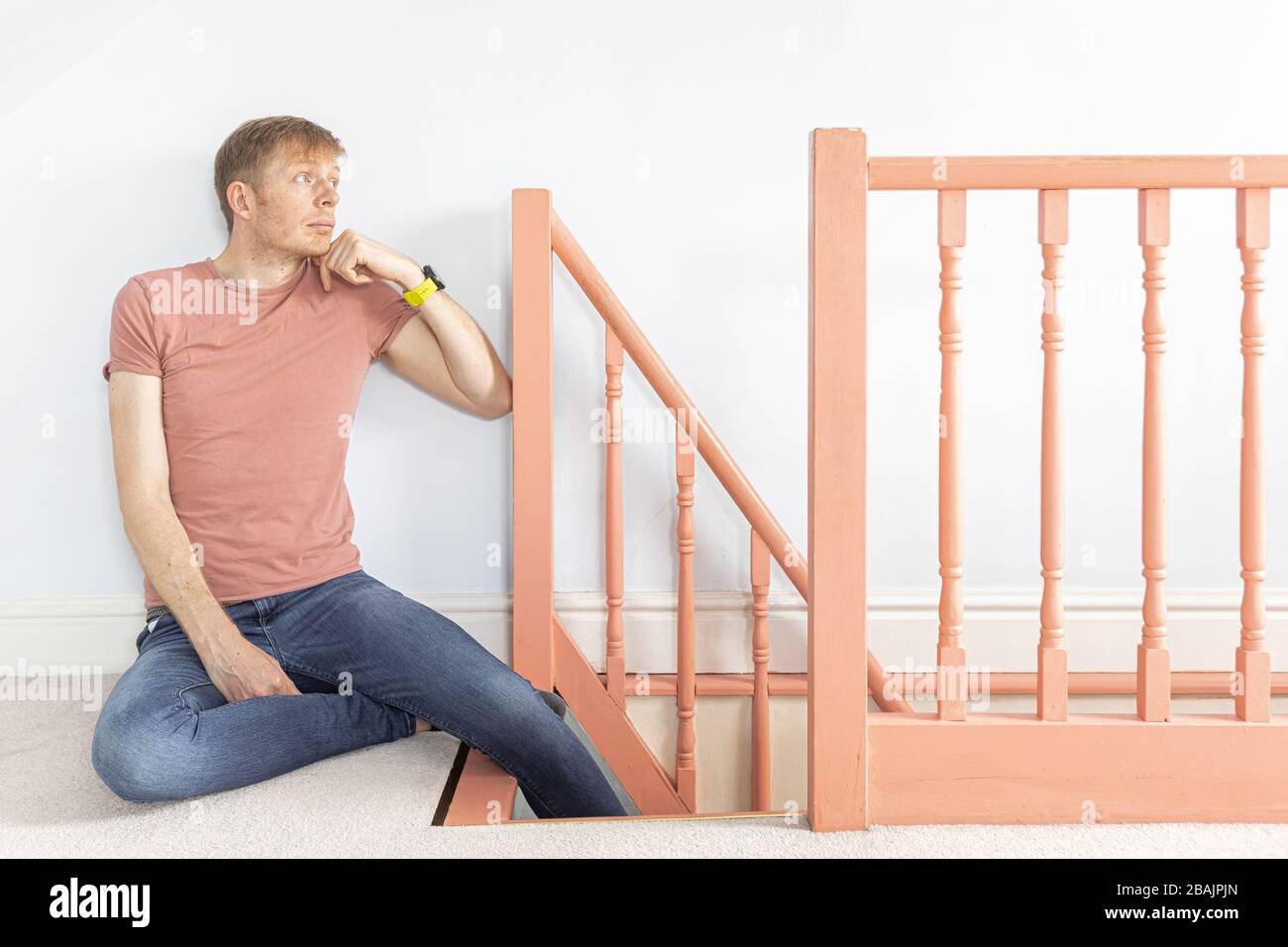 man in pink t-shirt sitting down leaning on banister thinking on top of the stairs Stock Photo