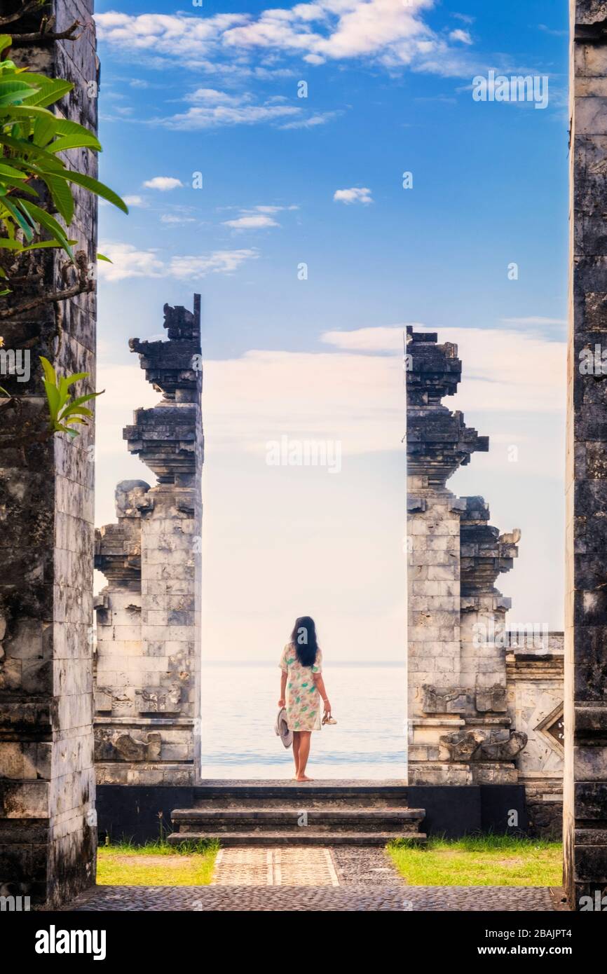 A woman stands between the stone gates to a Balinese temple, looking out to sea Stock Photo