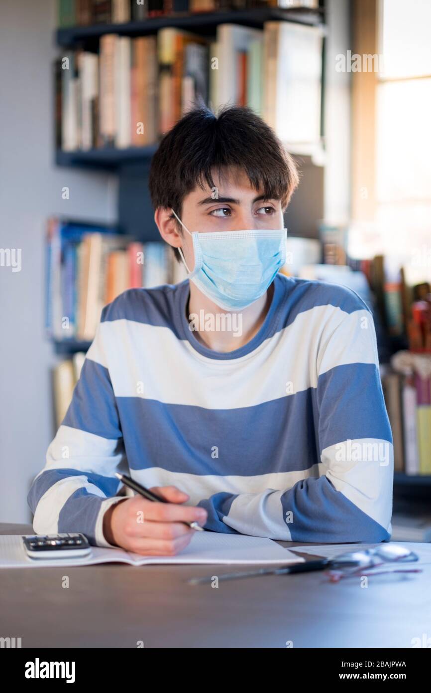 A college student wearing a mask and studying at home during a period of social distancing Stock Photo