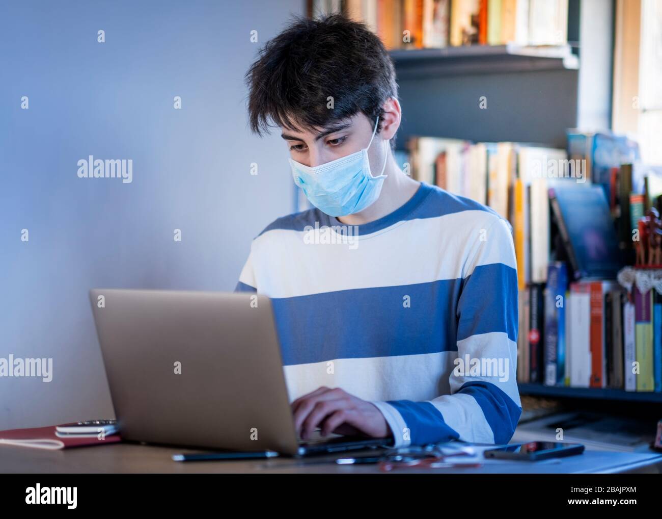 A teenager wearing a protective mask studying on their lap top at home Stock Photo