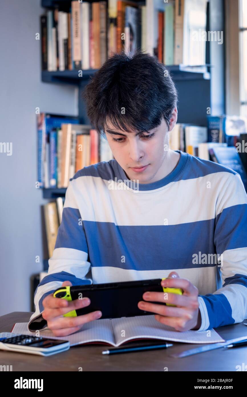 A teenager taking a break from study on his gaming console Stock Photo