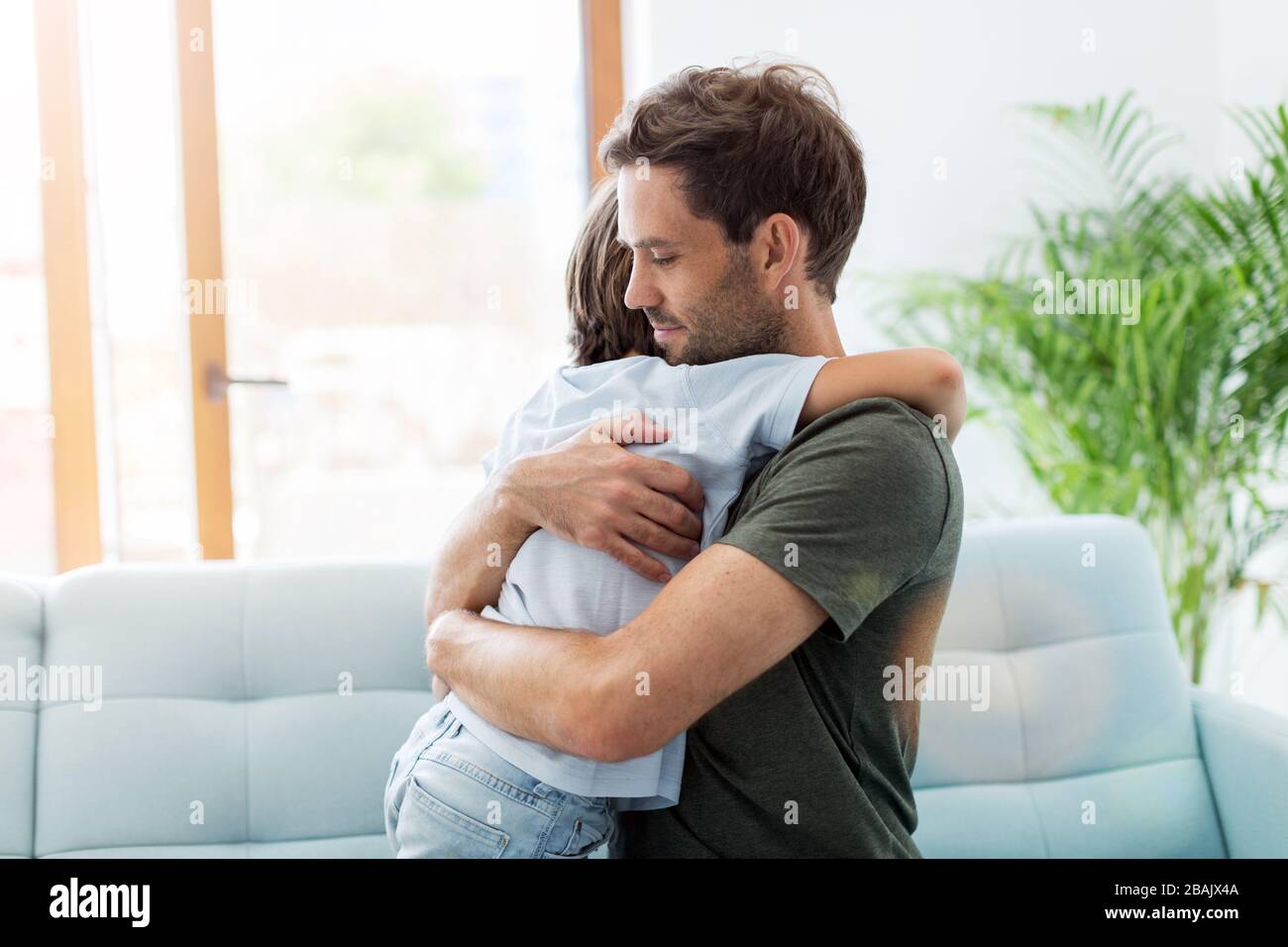 Father embracing son while sitting on sofa at home Stock Photo