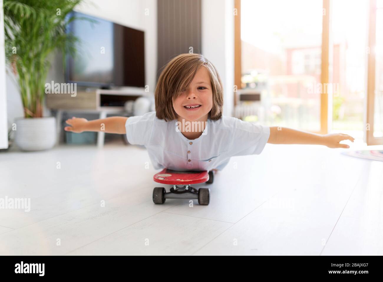 Boy with arms open lying on skateboard at home Stock Photo