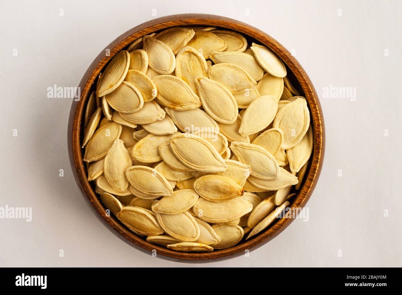 Unpeeled white color pumpkin seeds in bamboo bowl on white background. Stock Photo