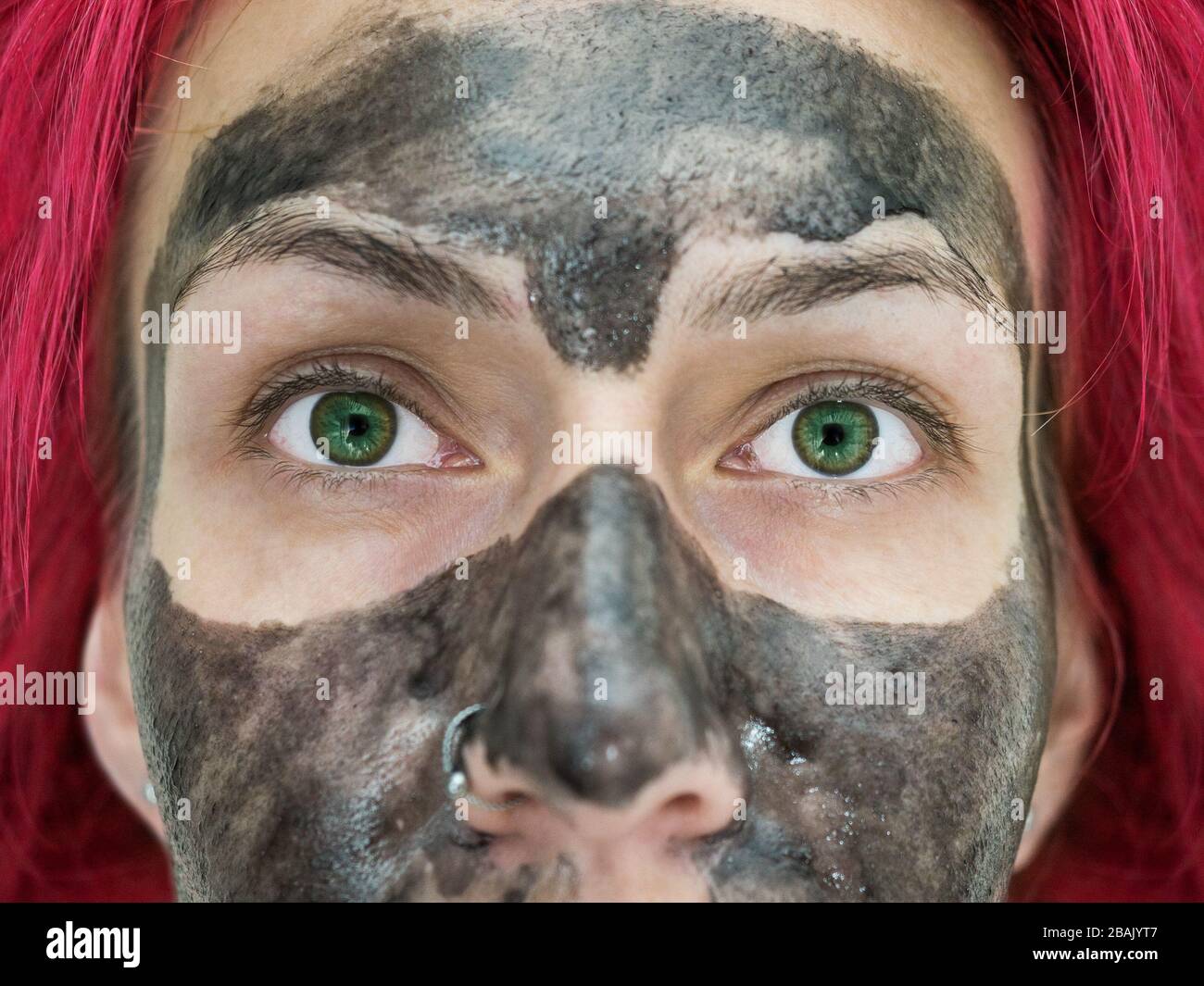 Close-up photo of a fragment of the face of a girl with bright green eyes, red hair and black peel off mask on her face Stock Photo