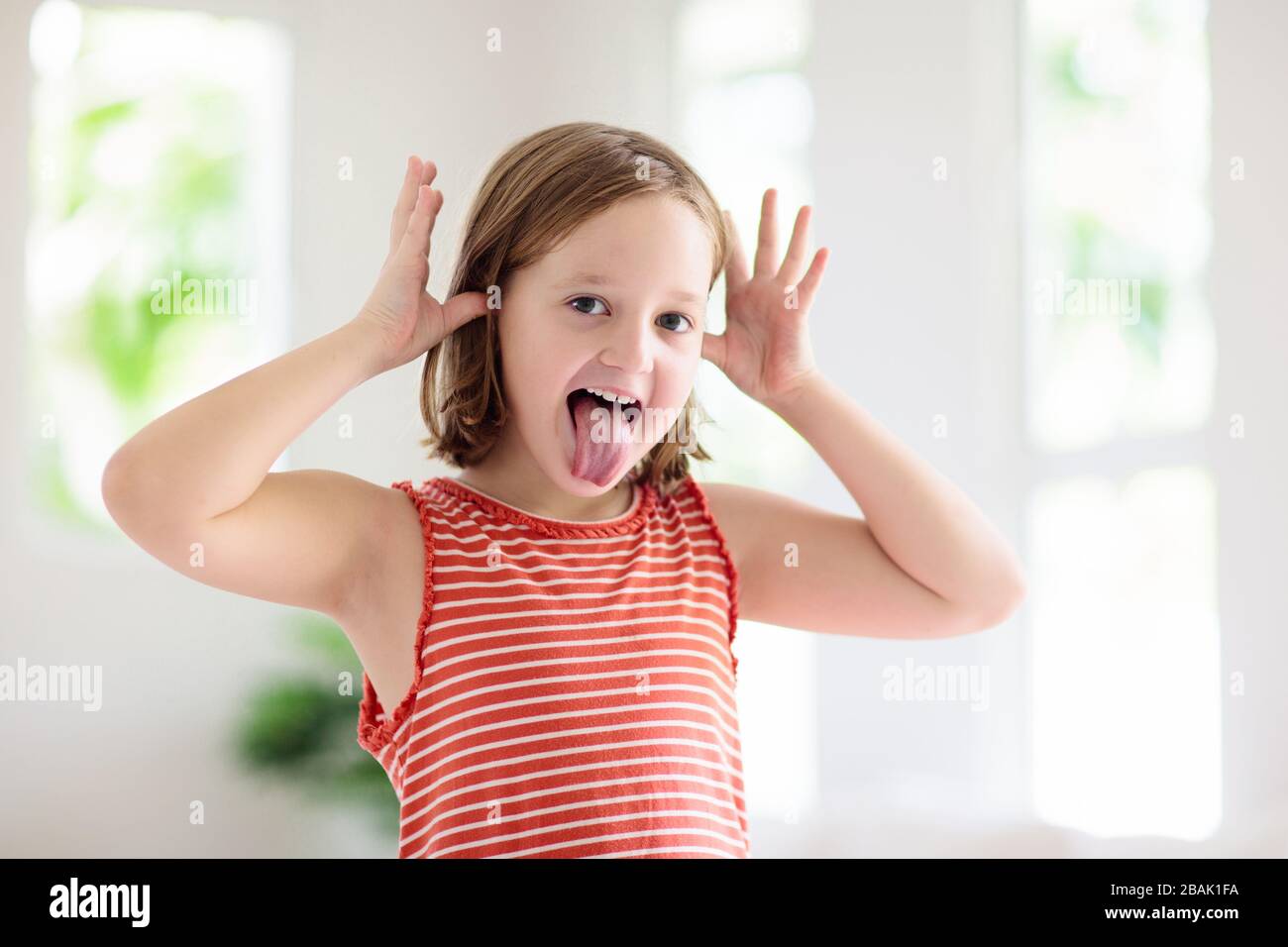 Child making funny face. Kid teasing and laughing. Silly little girl playing and smiling. Stock Photo