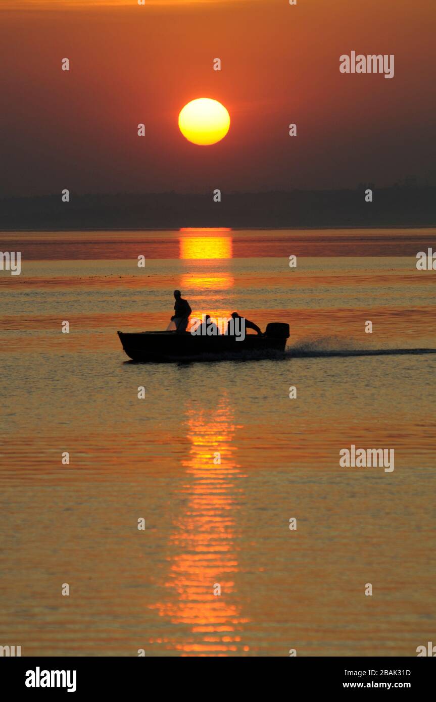 Red sunset on the still sea, black silhouette of boat with three men ...