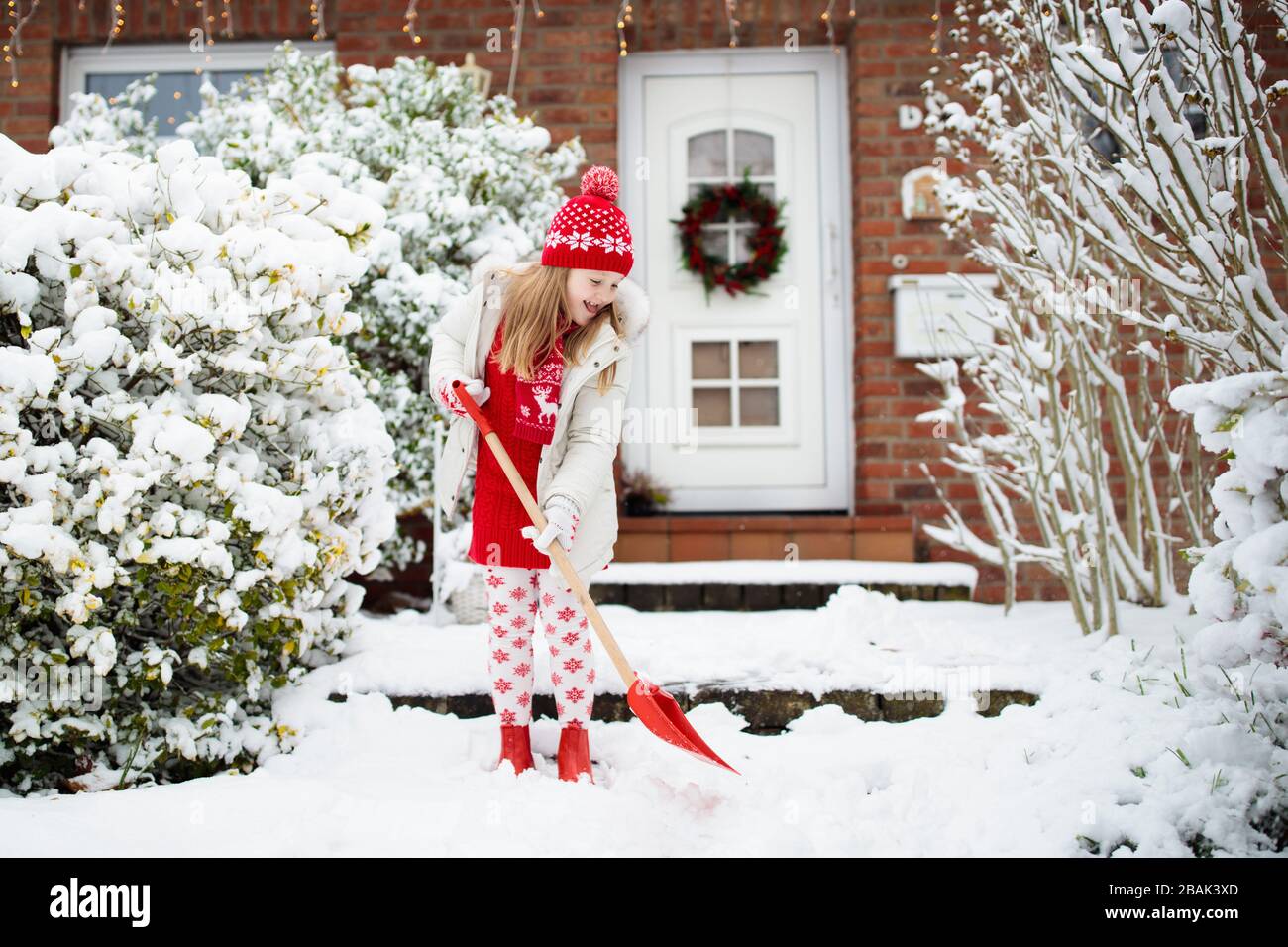 Child shoveling snow. Little girl with spade clearing driveway after winter snowstorm. Kids clear path to house door after Christmas blizzard. Snowfal Stock Photo