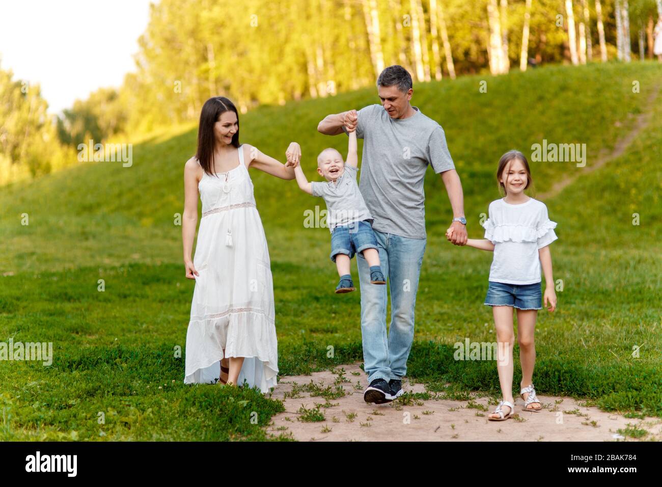 Mom, dad, son and daughter walk in the park at the weekend holding hands. Happy family in nature. fun big family in the forest. Stock Photo