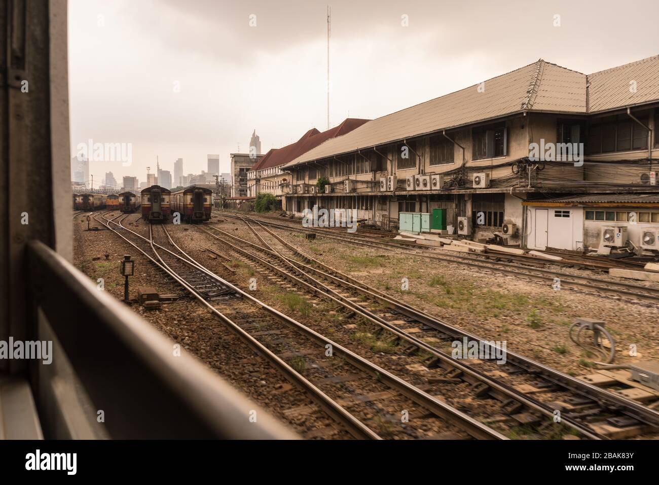 Trains on a hazy day in central train station. Skyscrapers in distance. Arrival from Don Mueang
