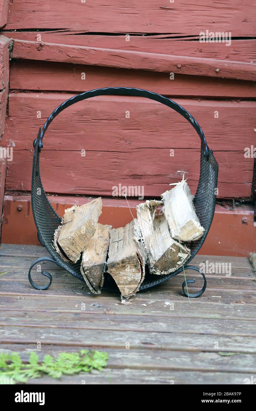 Firewood holder made of metal net. There is some firewood in the holder which is located on a wooden porch of a retro style summer cottage in Finland. Stock Photo