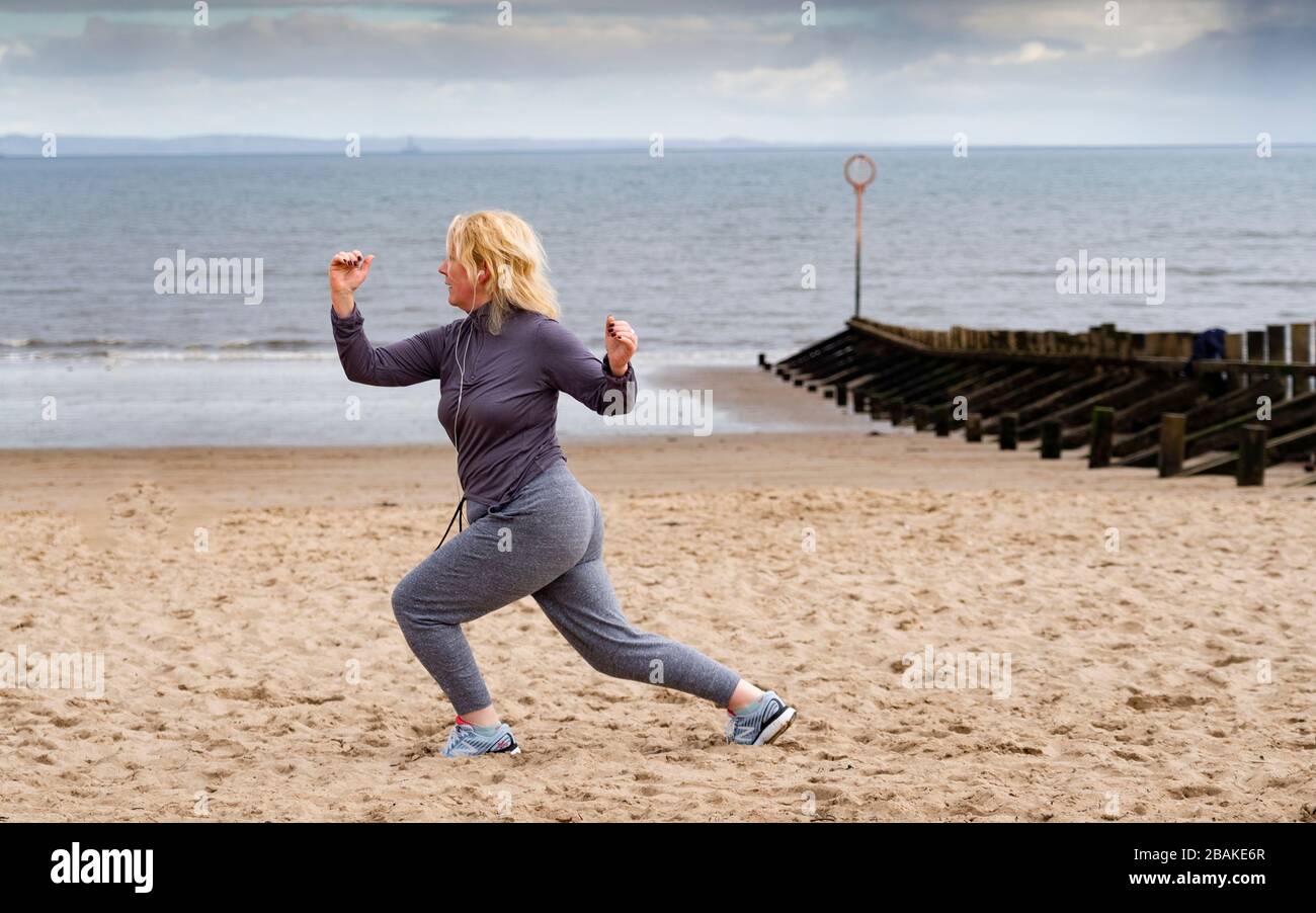 Portobello, Scotland, UK. 28 March, 2020. On the first weekend of the coronavirus lockdown the public were outdoors exercising and maintaining social distancing along Portobello beachfront promenade. Pictured; Annabel Meikle from Portobello working out on her special covid-19  solo training program set by her personal trainer. Iain Masterton/Alamy Live News Stock Photo