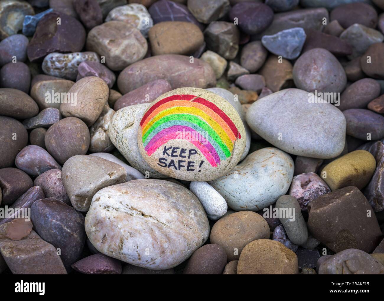 Pebbles painted with a rainbow and the words 'Keep Safe' written on it inside a garden in the UK as a message of hope during the coronavirus pandemic Stock Photo