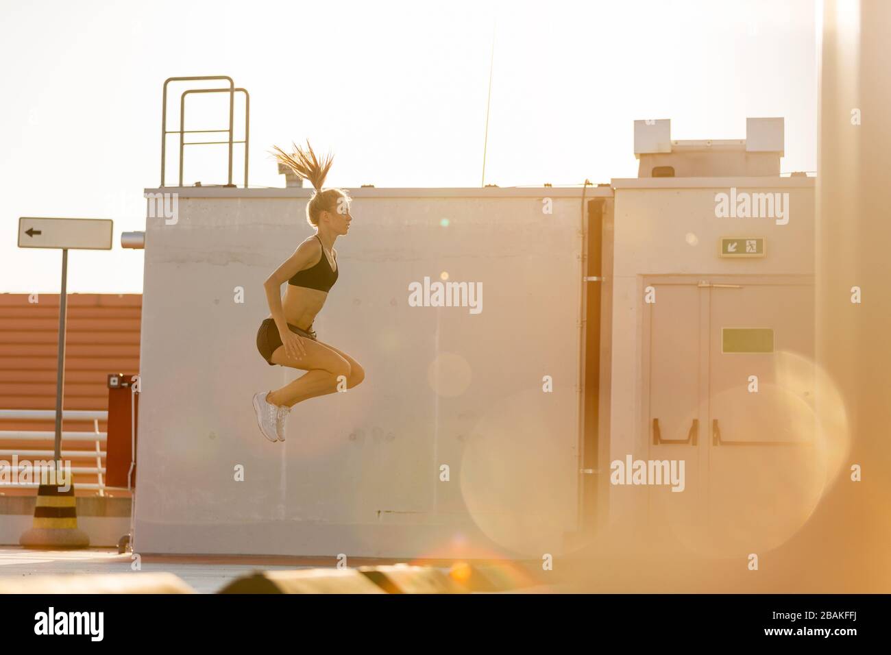 Young woman doing fitness exercise on parking level in the city at sunset Stock Photo