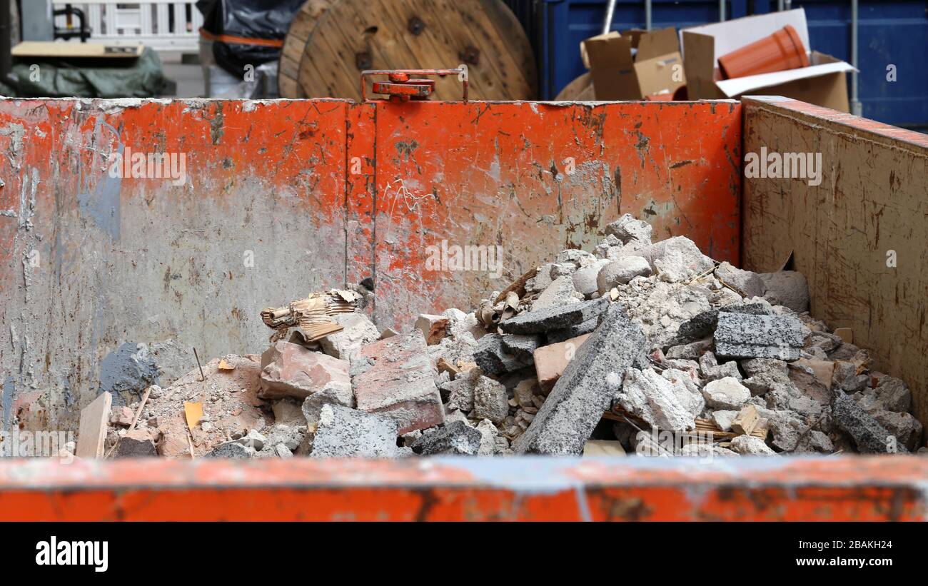 Orange colored dirty and rusty dumpster full of construction waste like broken tiles, cements, etc debris. Photographed in urban area in Helsinki. Stock Photo