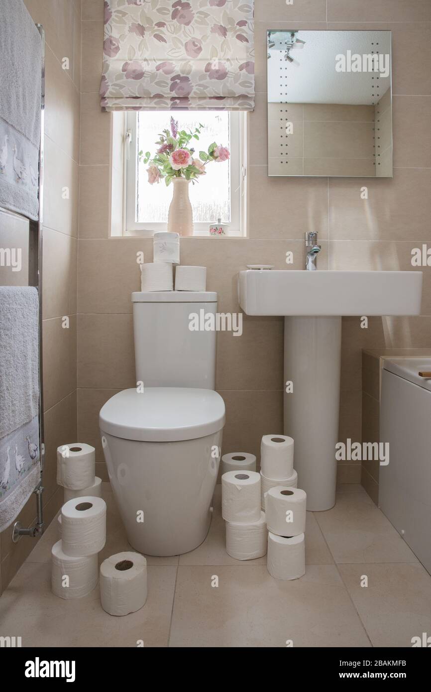 A home interior of a tiled bathroom with white suite and the toilet covered in toilet rolls after panic buying during the Coronavirus Pandemic Stock Photo