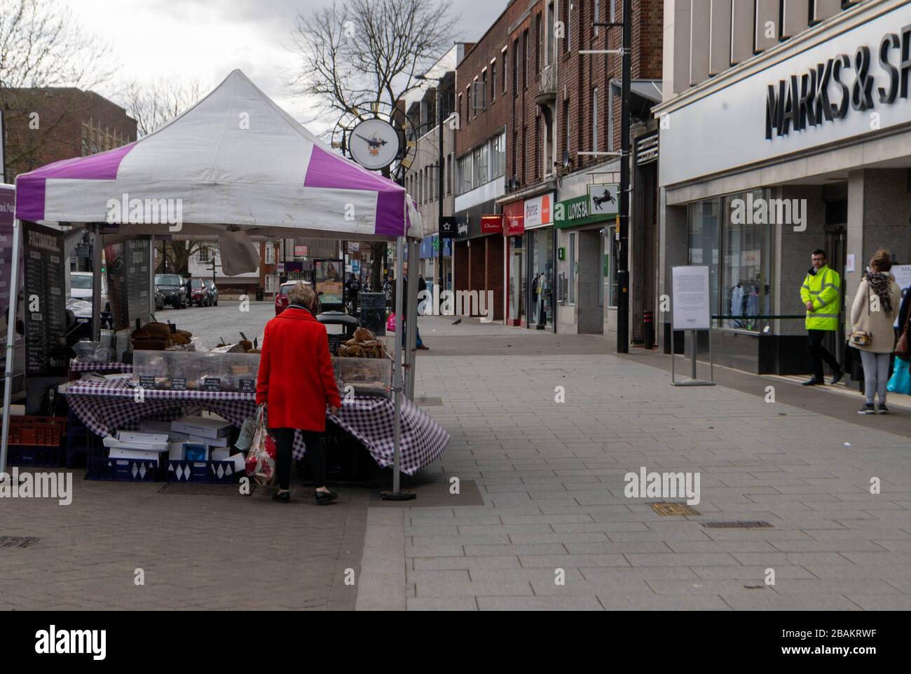 Brentwood Essex, UK. 28th Mar, 2020. A deserted Saturday afternoon High Street in Brentwood Essex as covid-19 social distancing regulations bite A solitiary market stall with a solitiary customer beside a line at Marks and Spenser Credit: Ian Davidson/Alamy Live News Stock Photo