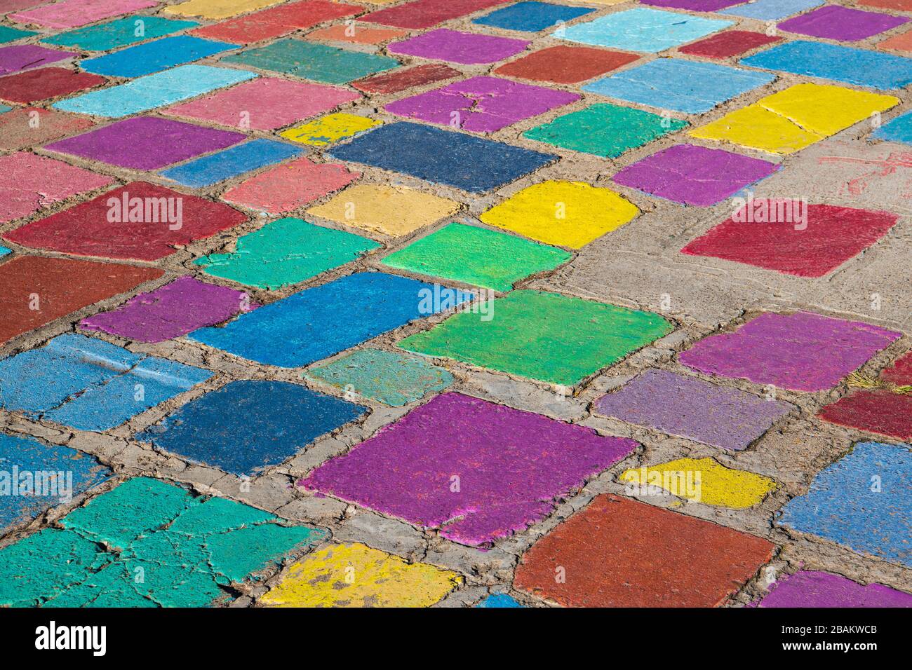 Rustic concrete tiles in a random pattern painted in vibrant hues of purple, green, blue, and red in an outdoor floor Stock Photo