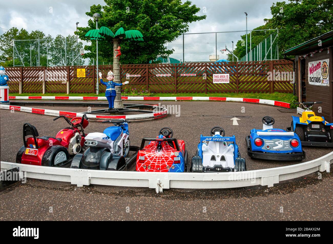 A plastic policeman is located in the centre island of a fun racing circuit for children as small imitation race bikes and cars wait for customers Stock Photo