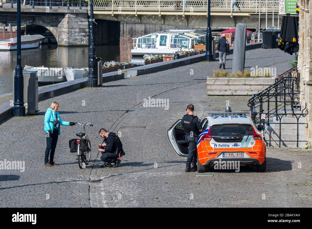 Two policemen / police officers checking elderly cyclist due to the 2020 COVID-19 / coronavirus / corona virus pandemic in Flemish city Ghent, Belgium Stock Photo