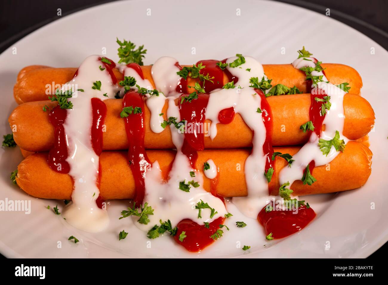 Boiled sausages with ketchup, mayonnaise and herbs on the plate Stock Photo