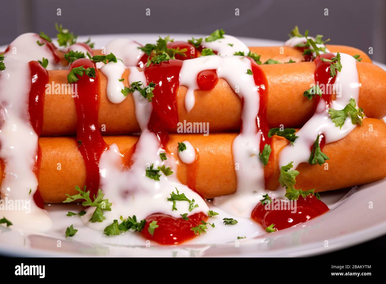 Boiled sausages with ketchup, mayonnaise and herbs on the plate Stock Photo