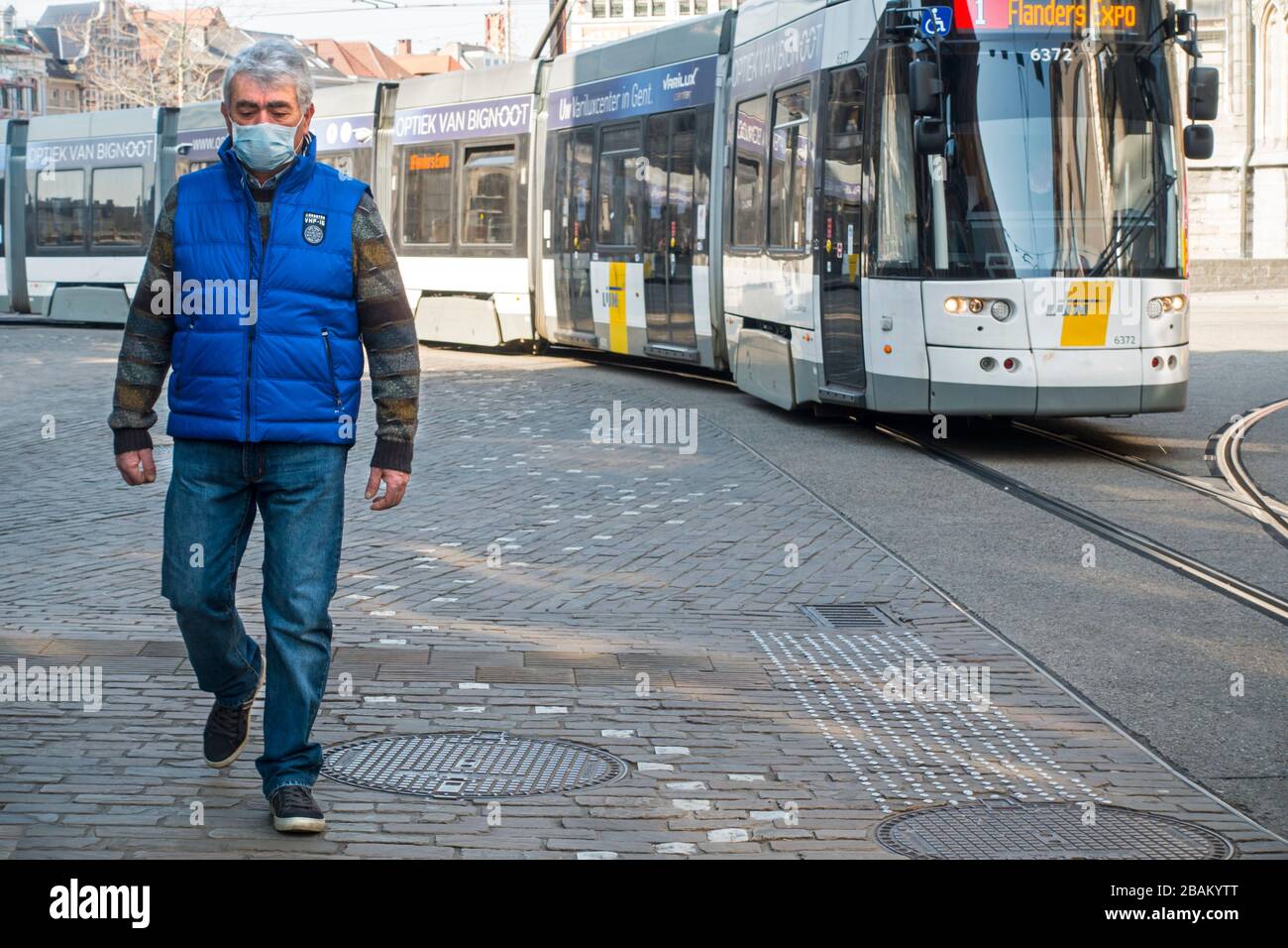 Tram and man wearing medical face mask due to 2020 COVID-19 / coronavirus / corona virus pandemic while walking in the Flemish city Ghent, Belgium Stock Photo