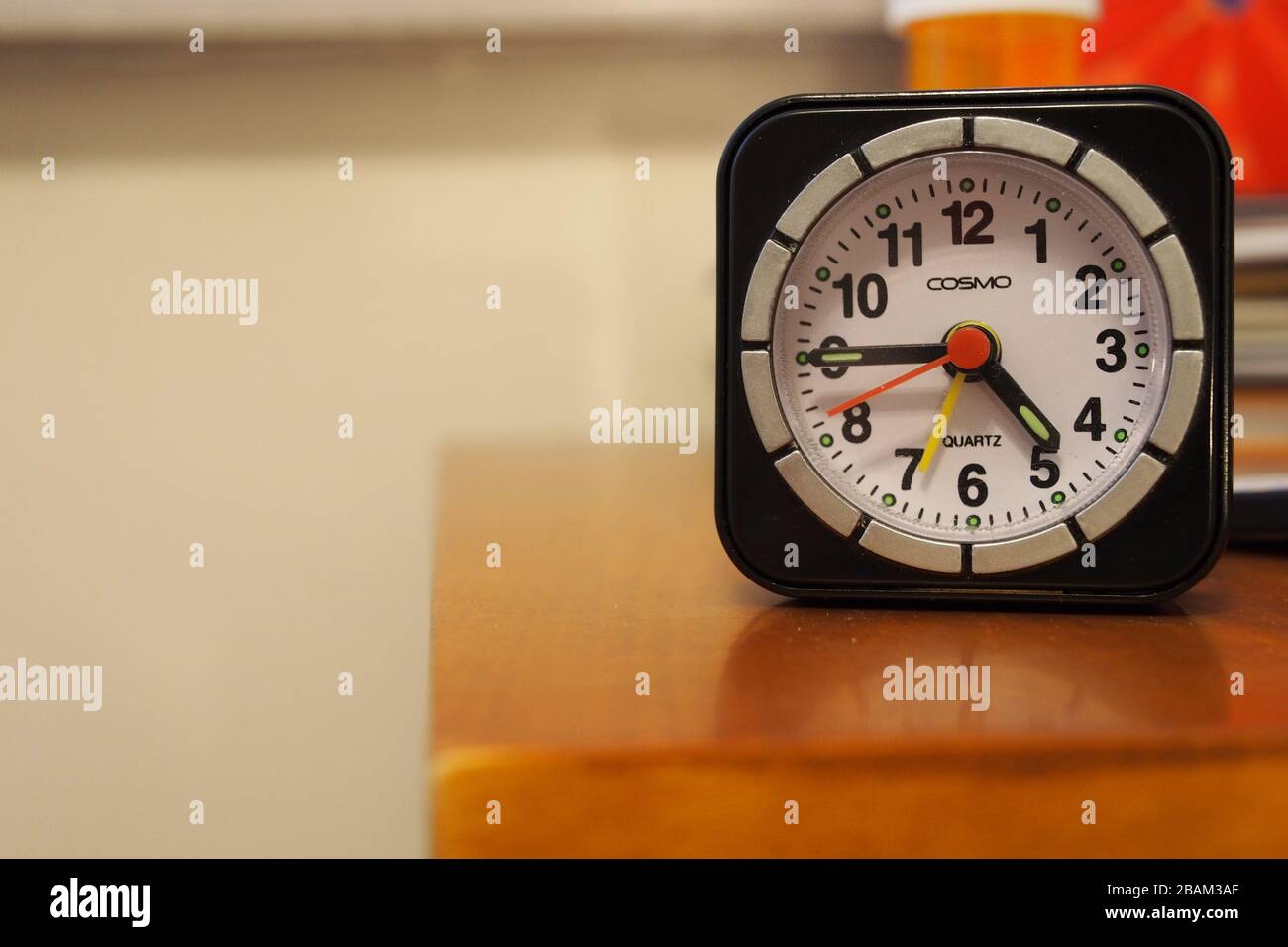 My cheap COSMO travel alarm clock on the bedside table. Current time 4:45pm. Alarm set for 7. Excellent little clock, for the price. Stock Photo