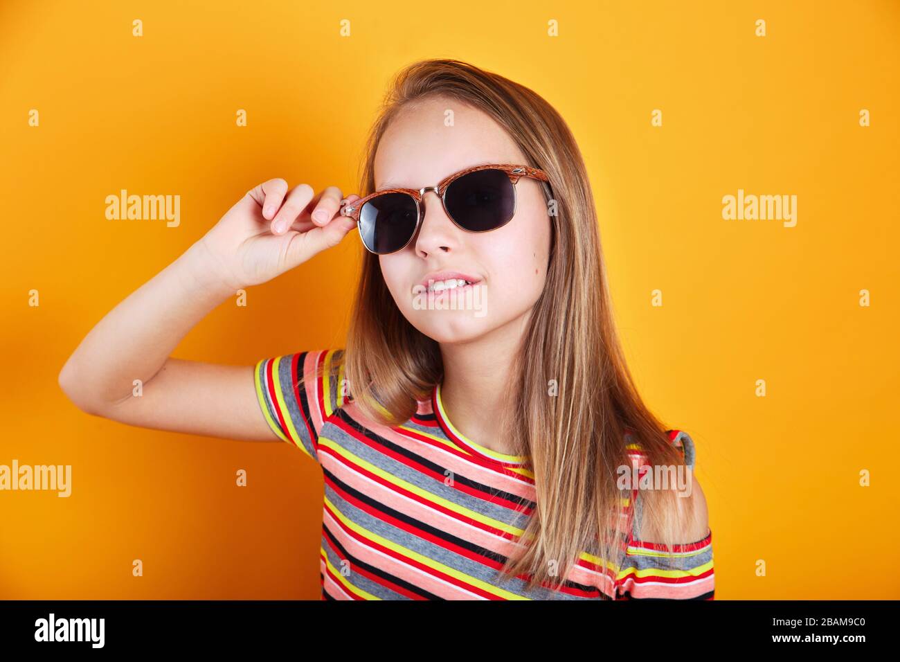 Close-up of trendy little girl in summer clothes and sunglasses on yellow background Stock Photo