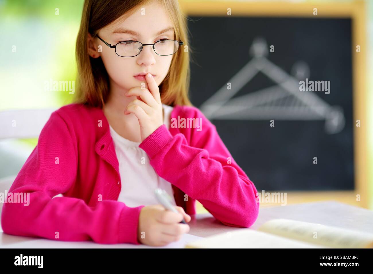 Smart schoolgirl studying with a pile of books on her desk. Young girl ...