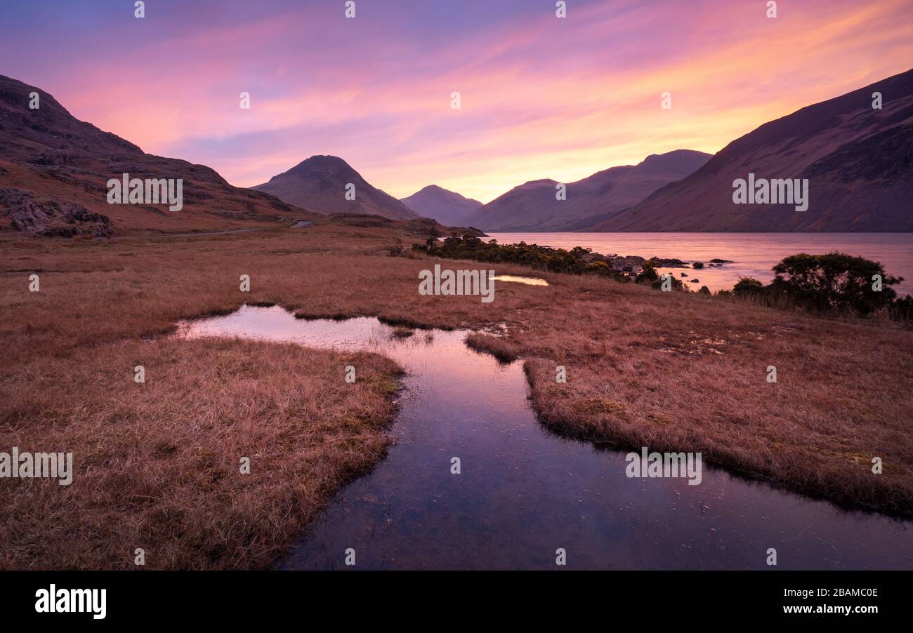Vibrant sunrise colour spreads across the valley of Wasdale in the English Lake District, with imposing high fells forming an imposing backdrop. Stock Photo