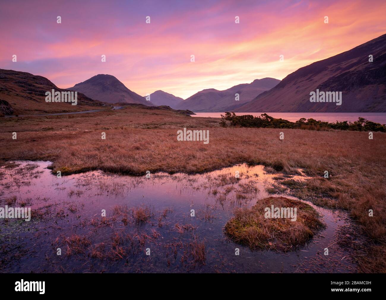 Vibrant sunrise colour spreads across the valley of Wasdale in the English Lake District, with imposing high fells forming an imposing backdrop. Stock Photo