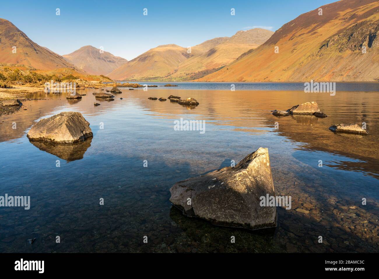 The high fells of the English Lake District are reflected in Wast Water on a calm spring afternoon with a completely clear blue sky. Stock Photo