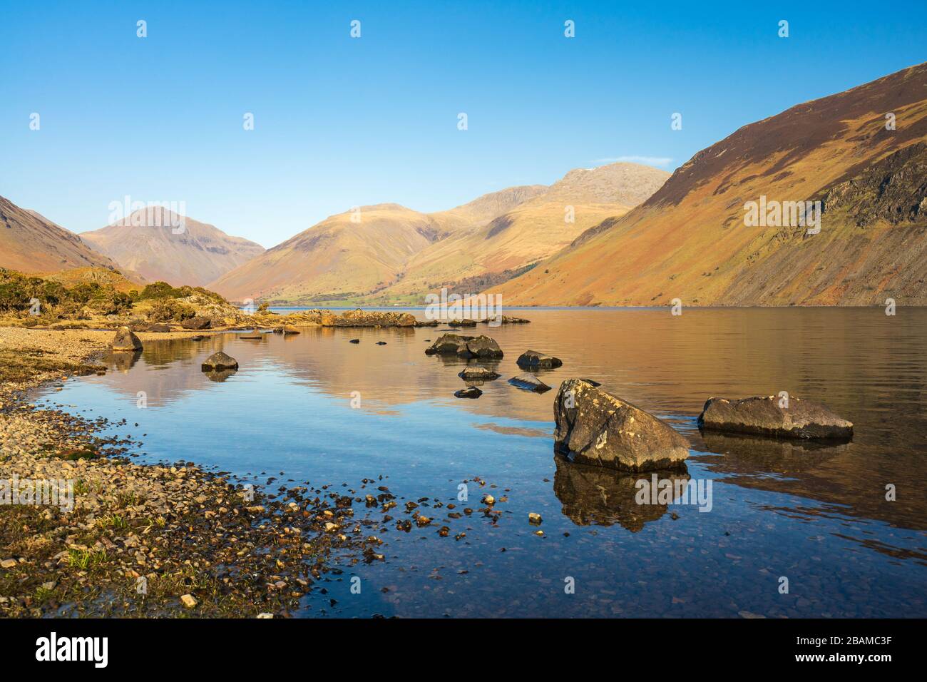 The high fells of the English Lake District are reflected in Wast Water on a calm spring afternoon with a completely clear blue sky. Stock Photo