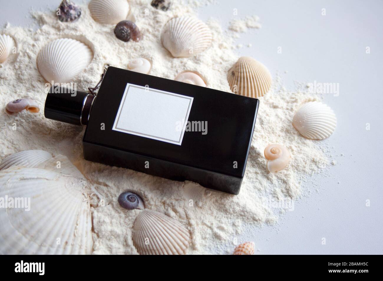 Black glass perfume bottle on white sand with seashells Stock Photo