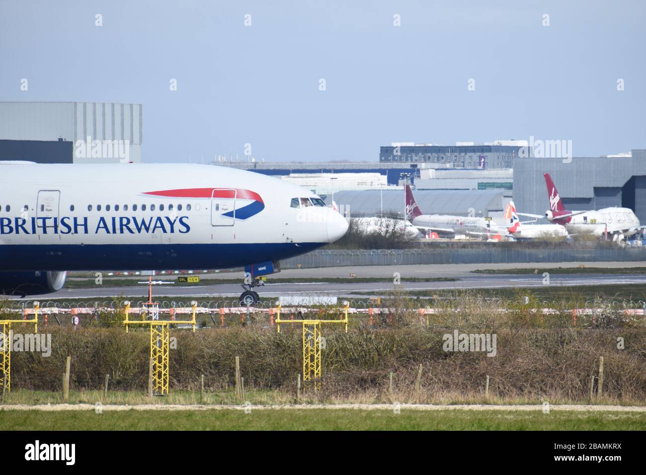 A British Airways Boeing 777-236 moves towards the runway for takeoff at Gatwick Airport, passing in front of some grounded Virgin aircraft. Stock Photo