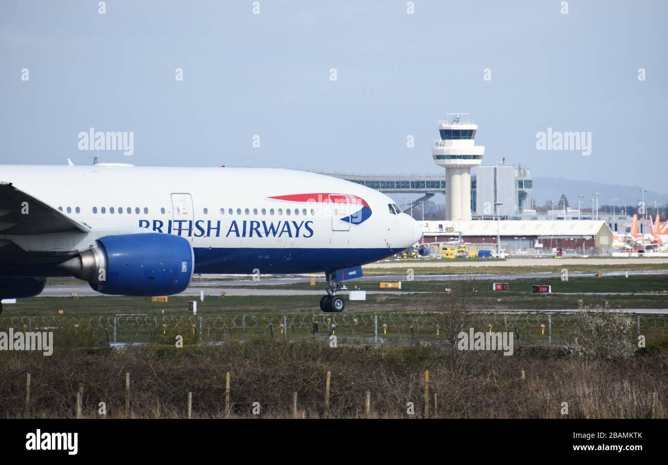 A British Airways Boeing 777-236 callsign G-YMME moves towards the runway for takeoff at Gatwick Airport, passing in front of the air traffic control. Stock Photo